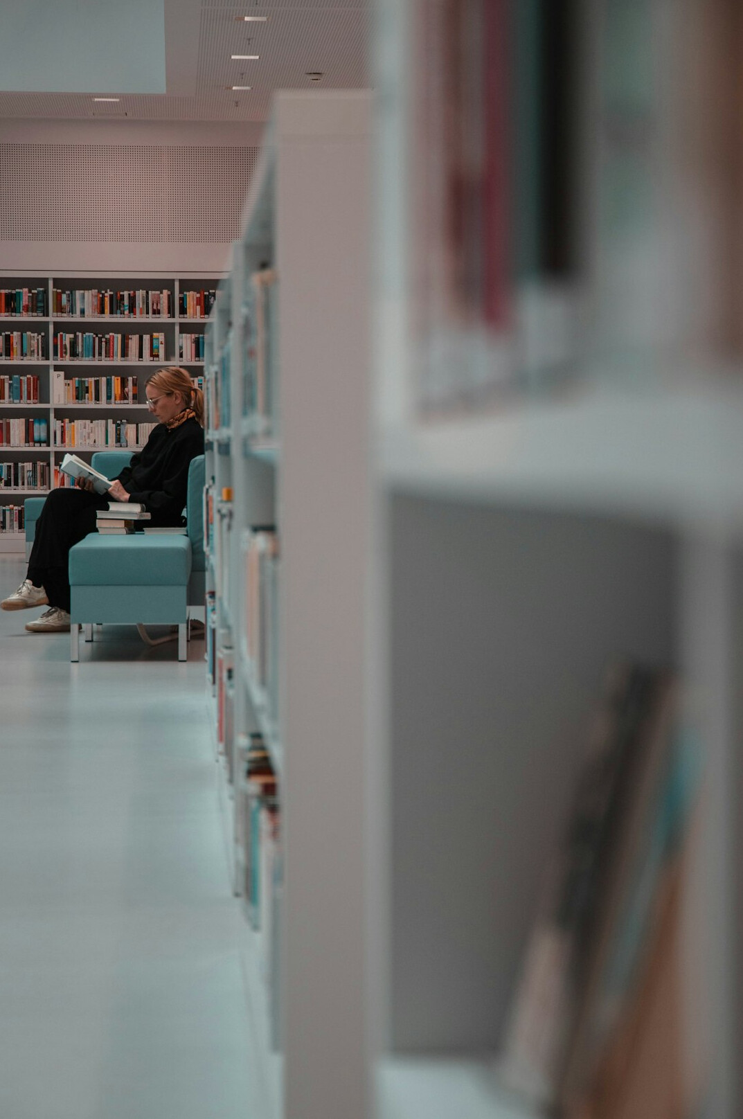 Person reading a book in a quiet library with a laptop nearby